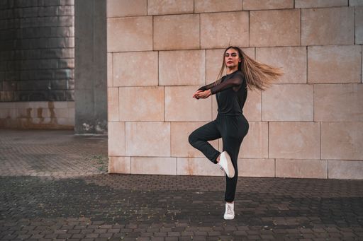 A young ballerina in a black suit does ballet pirouettes on the street. Contemporary street dance concept.