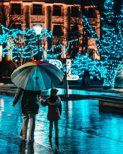 A vertical shot of a female and a child holding an umbrella on a sidewalk at night