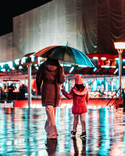 A vertical shot of a female and a child holding an umbrella on a sidewalk at night
