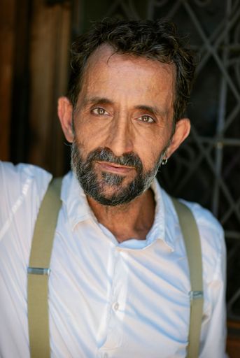 A vertical portrait of a Hispanic middle-aged man wearing a white shirt