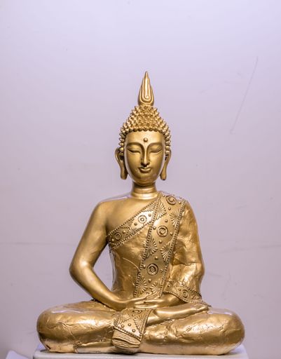 A vertical shot of a golden Buddha statue in white and blue background