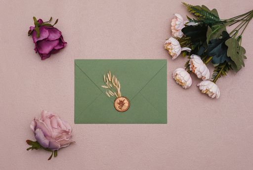 A top view of aesthetic green wedding card envelope and beautiful flowers on light pink surface