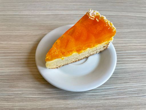 Closeup shot of a delicious tangerine jelly cake with cream and shredded coconut on a white plate lying on a wooden table.