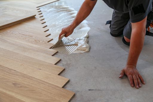 A male worker installing a wooden laminate flooring on his knees