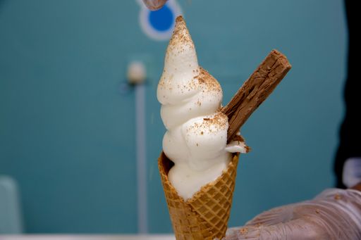 A close up of a man adding chocolate topping on a vanilla ice cream cone
