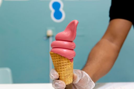 A man holding a strawberry ice cream cone in his hand on a blue background