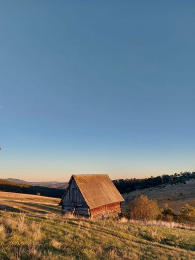 A vertical shot of an old wooden house in the mountains on a cloudless day