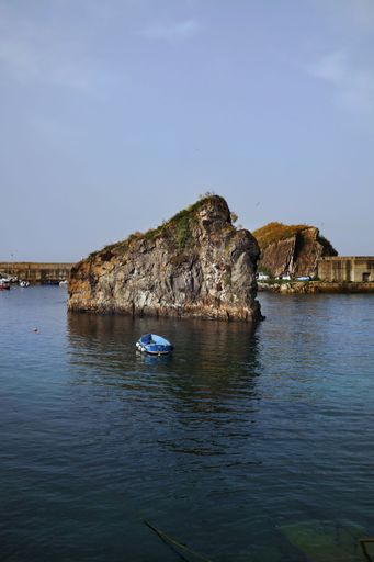 A vertical shot of a huge rock and a fishing boat in the Cantabrian  sea in Cudillero in Asturia Spain