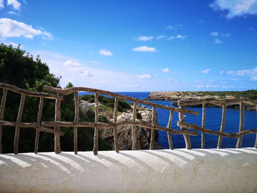 a beach in Binibeca (Menorca) seen through wooden railing of a balcony