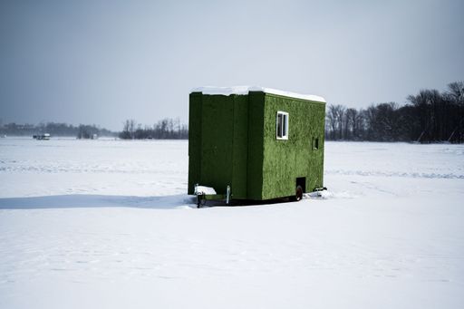 A green ice fishing hut on a frozen lake with on a sunny winter day