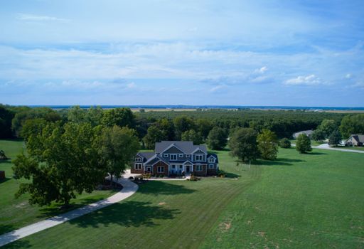 Aerial view of a very nice house with green farmland and lush trees under blue sky