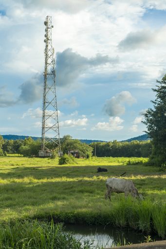 A vertical shot of a telecommunications tower in a large green field under the beautiful sky during daylight