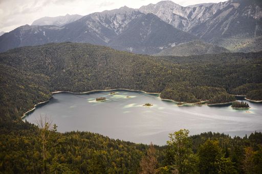 A high angle shot of a small lake surrounded by green plants on a mountain range