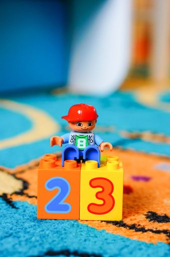 Lego Duplo boy figurine sitting on a plastic block with number