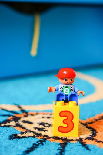 Lego Duplo boy figurine sitting on a plastic block with number