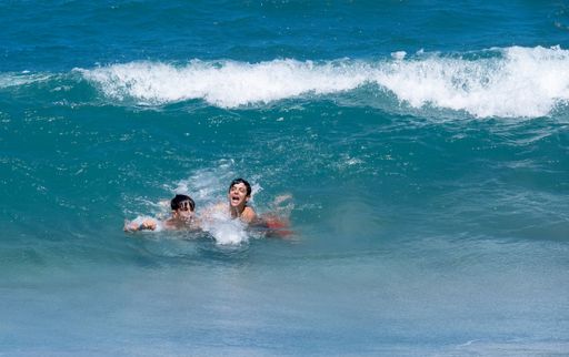 two teenagers have fun on the beach playing with big waves in the blue water on a summer day