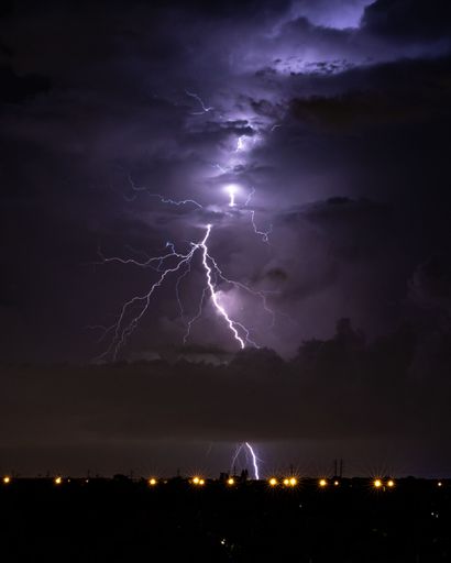 A vertical shot of bright and flashing lightning, lighting up the sky at night