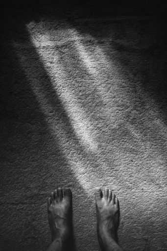 A black and white vertical shot of feet of a man standing on the stone ground