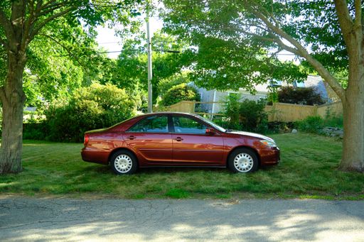 A view of a red car parked on grass in a garden with trees