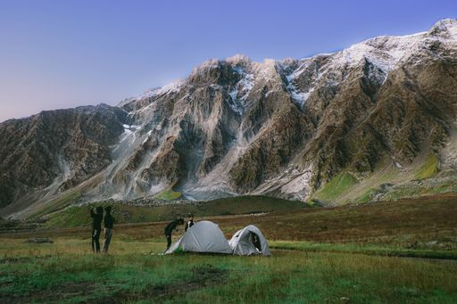 A group of young hikers setting up tents and taking photos in a meadow with snowy mountains in the background