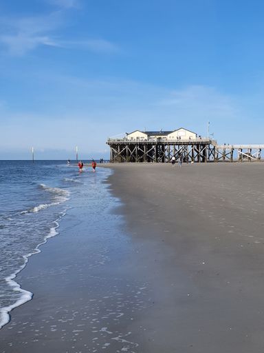 A vertical of a wooden jetty on the waters of the North Sea in St. Peter-Ording against the blue sky