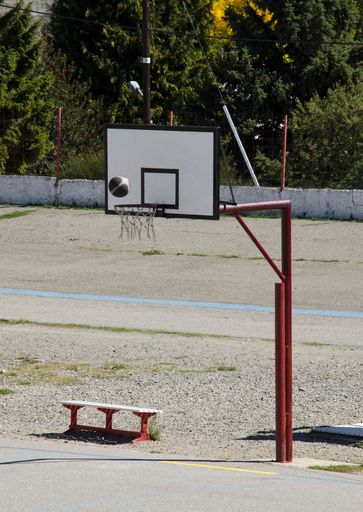 A basketball court in a park, with the hoop and the ball in the air