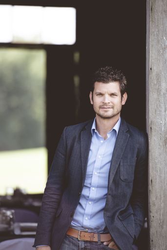 A vertical shot of a well-dressed male leaning against the wall and looking at the camera