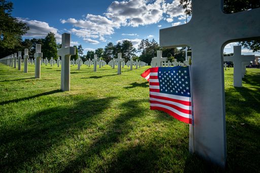 An American flag standing at the gravestone of a killed soldier at the war cemetery in Normandy