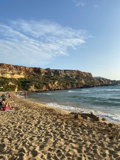 A vertical shot of people at a beautiful beach surrounded by cliffs captured from a sandy shore