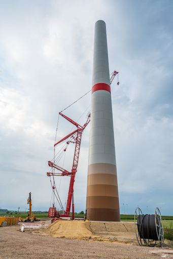 A vertical shot of a wind turbine at the construction site under blue cloudy sky