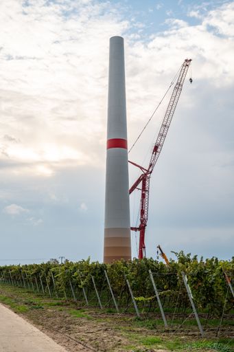 A vertical shot of a wind turbine at the construction site under blue cloudy sky