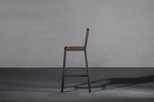 A closeup of a modern chair with high legs in a room against a gray wall