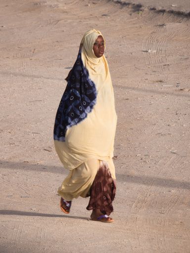 A vertical shot of a Muslim black woman walking down the street in Nouakchott