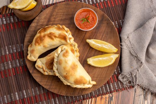 A top view of the Argentinian homemade empanadas on wooden plate with red sauce and lemon slices
