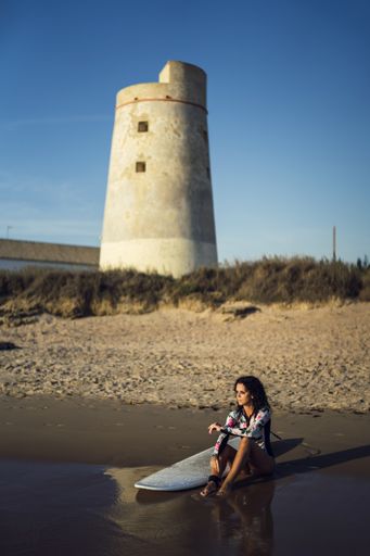 A vertical shot of a female and her surfboard by the lighthouse