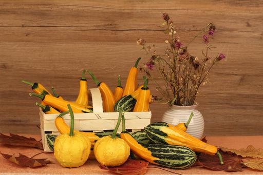 A basket full of pumpkins and a flower vase on a wooden background
