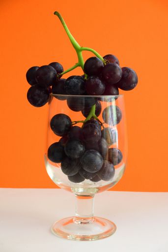 A vertical closeup of grapes in a glass on an orange background