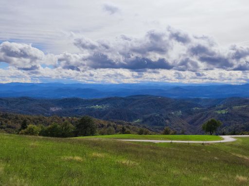 A beautiful scene of green meadows with green mountains and cloudy sky on the horizon