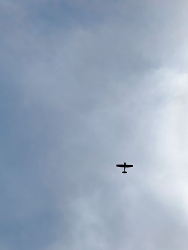 A vertical shot of a plane flying in the cloudy sky
