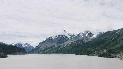 A beautiful scene of icy Tibet Mountain by frozen water under white cloudy sky