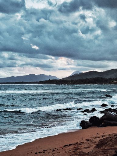 A vertical shot of sea waves hitting the shore on a cloudy day