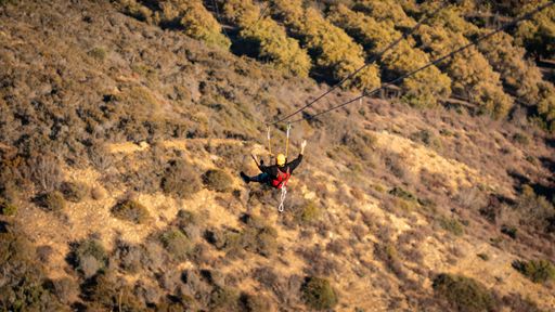 A back view of human flying with zipline over greenery mountains