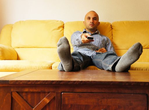 A lazy male sitting on the sofa with his feet on the table and holding a remote