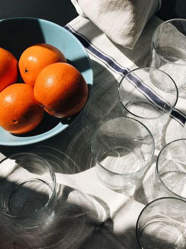 A vertical of glass cups and oranges on a blue plate on white background