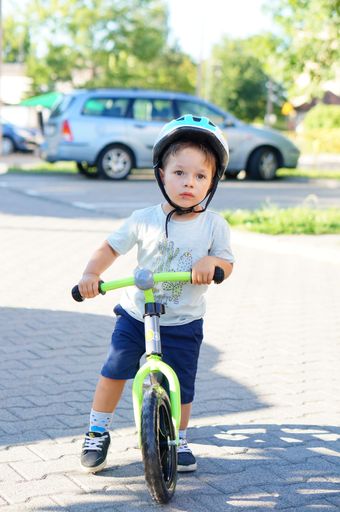 Young boy on a running bike wearing a safety helmet on a street