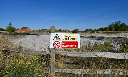 A dried up pond with "no swimming" and "danger" signs  under the blue sky