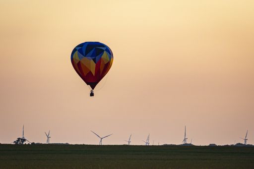 Dramatic gorgeous mosaic colorful balloon where aeronaut boldly flies and lands near wind farm of many turbines in an open pasture.