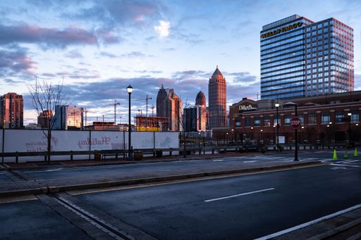 This image is of a busy city street lined with tall skyscrapers, buildings, and a parking lot