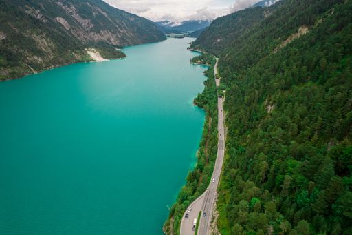 An aerial view of a road by Achen Lake between lush green steep mountains in Austria