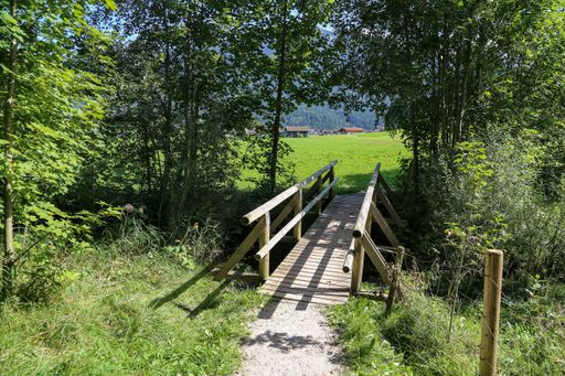 A wooden bridge over a small mountain river surrounded by green nature during daylight